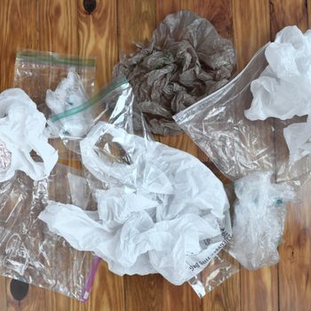 Plastic bags lie scattered on a wooden floor, showing various crumpled textures and translucent surfaces.
