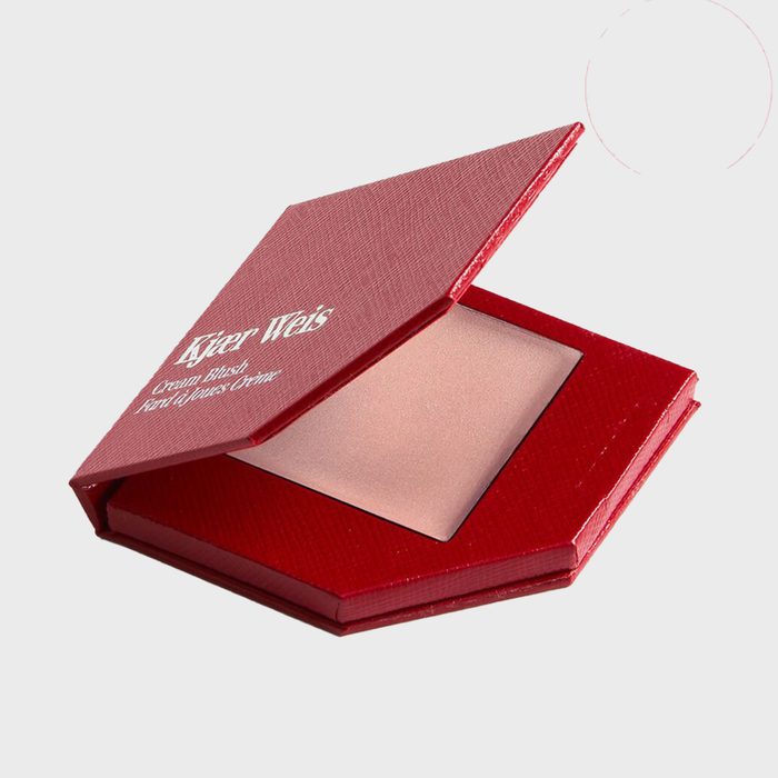 Compact case opens, revealing blush inside; red texture surrounds in a minimalist setting. Text reads, 