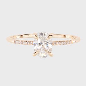 A gold ring features an oval diamond centerpiece and smaller diamonds on the band, set against a plain white background.