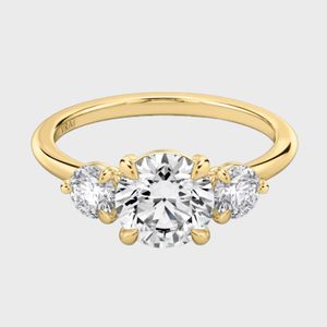 Gold ring features three sparkling diamonds, with a larger central stone, set on a plain band against a white background.
