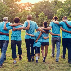 People in blue shirts walk with arms linked in a grassy park at sunset.