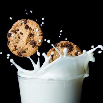 Cookies splash into milk, creating droplets in mid-air, against a dark background.