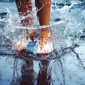 Feet splash water in a puddle, creating dynamic, clear water arcs against a wet surface.
