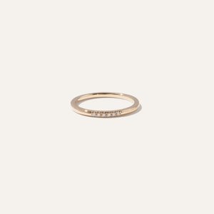 A thin gold ring, adorned with small diamonds, rests centered on a plain white background.
