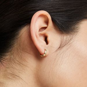 Gold earring hangs from an ear, surrounded by dark hair and skin, creating a simple, elegant appearance.