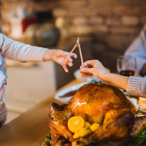Child and adult pull a wishbone over a roasted turkey on a family dining table.