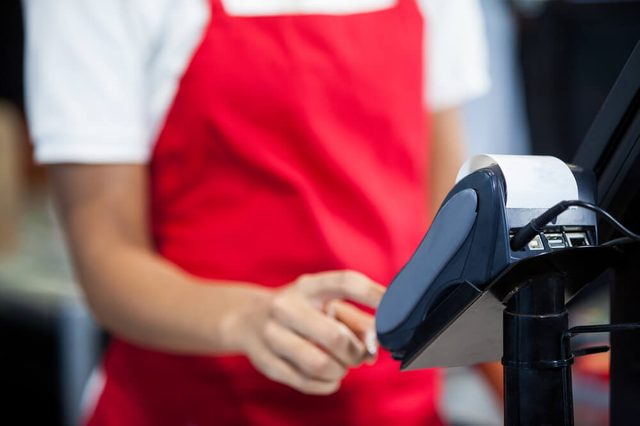 Mid section of female staff using credit card terminal at cash counter in supermarket