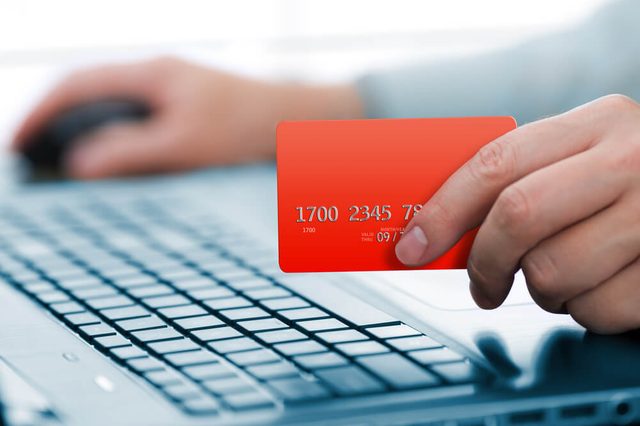Man holding credit card in hand and entering security code using laptop keyboard