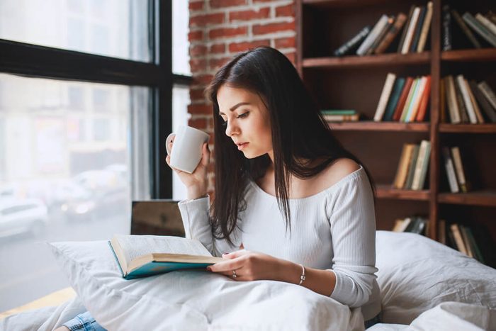 Woman reading book with cup of coffee at home in the living room