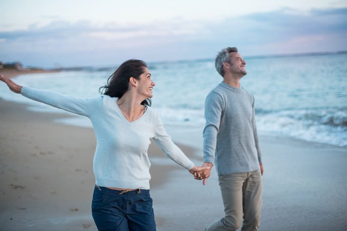 Beautiful couple walking on the beach at sunset. They are barefoot and wearing casual clothes