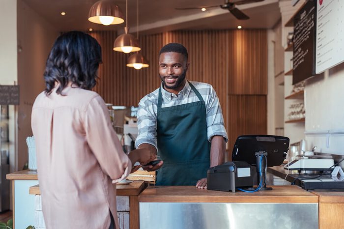 Smiling barista using nfs technology to help a customer pay for a purchase with their smartphone in a cafe 