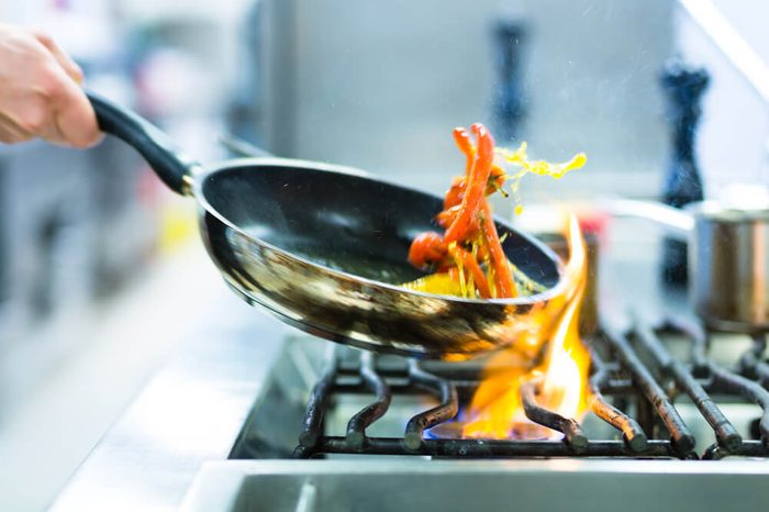 Chef in restaurant kitchen at stove with pan, doing flambe on food