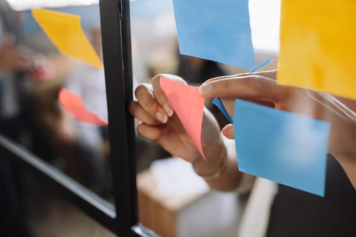 Close up shot of hands of woman sticking adhesive notes on glass wall in office