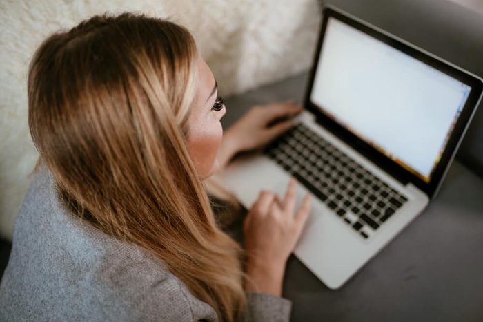 Beautiful young woman laying down on bed and using laptop. She is surfing on the net and checking social media.