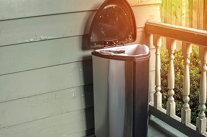 Trash on home porch. Smelly garbage bin outside for removal from house. Room for copyspace.