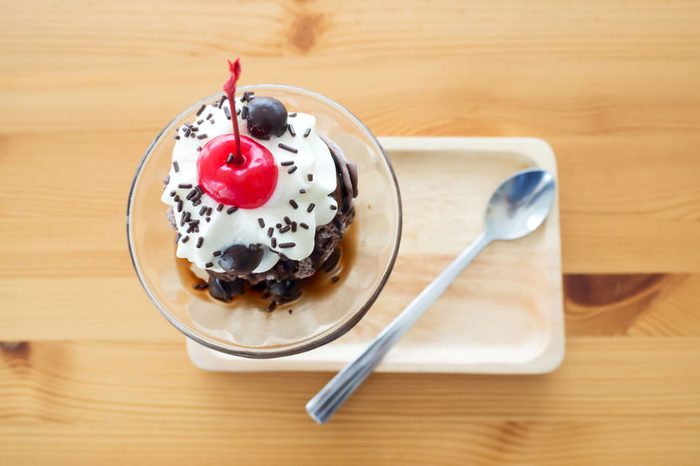 Chocolate sundae ice cream served with whipping cream and cherry on top. Pour chocolate sauce and chocolate ball. On wooden tray. Top view.