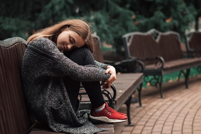 Young female with blond hair sitting on the bench in the park. Positive teenage girl dreaming on the bench. Cold autumn weather. Art concept