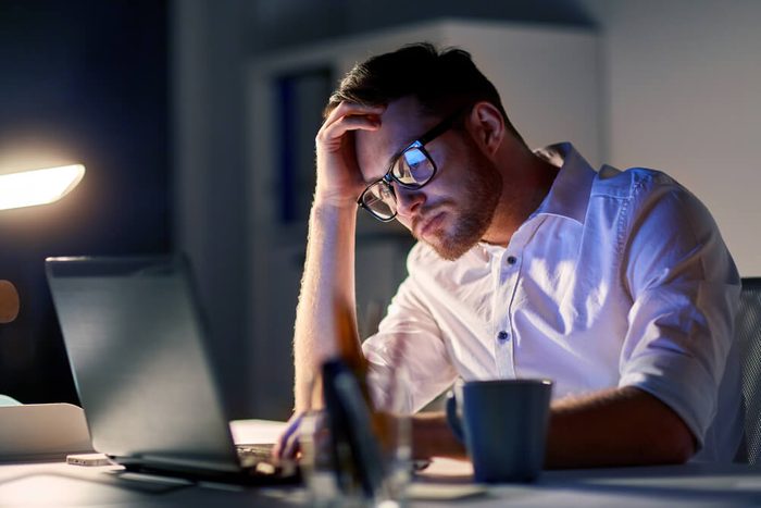 business, overwork, people, deadline and technology concept - stressed businessman in glasses with laptop computer thinking at night office