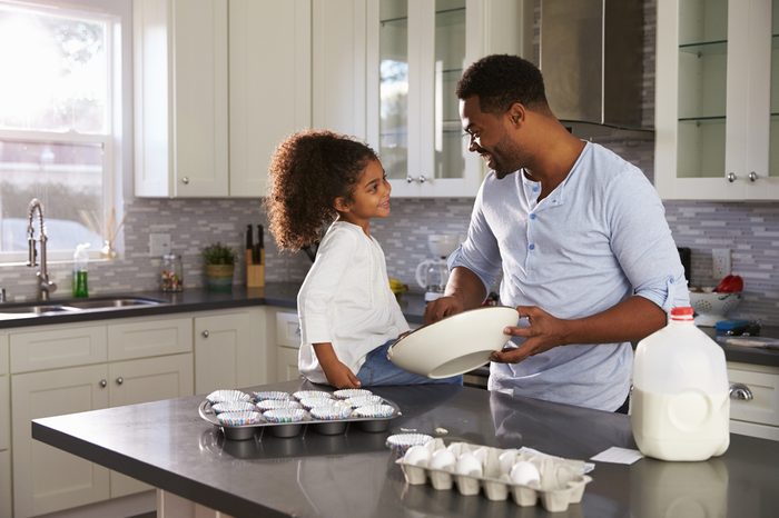Black dad and young daughter look at each other while baking
