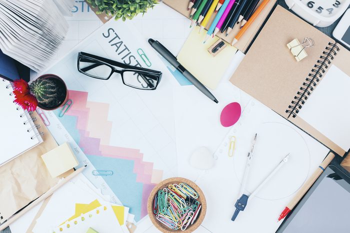 Top view of messy office workplace with business report, glasses, cactus, tablet and various stationery items