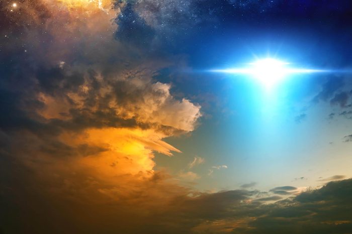 Fantastic background - bright light from extraterrestrial aliens spaceship, ufo in red glowing sunset sky. Elements of this image furnished by NASA