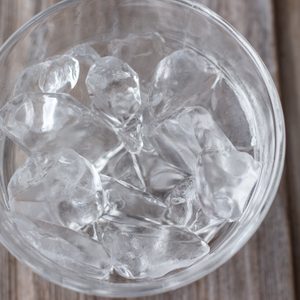 Ice cubes fill a transparent glass sitting on a wooden table.