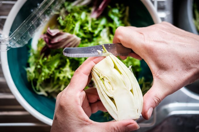 Middle aged female hands cutting fennel over salad bowl. Top down view.