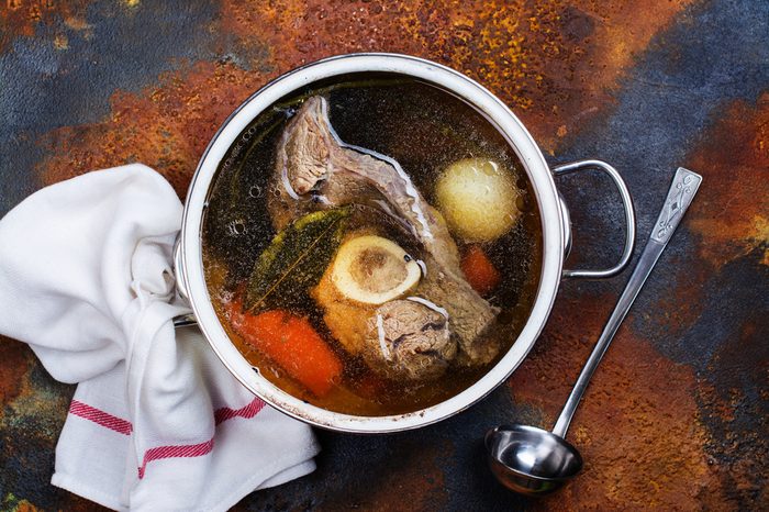 Broth soup in a cooking pot with ladle on dark stone background. Top view