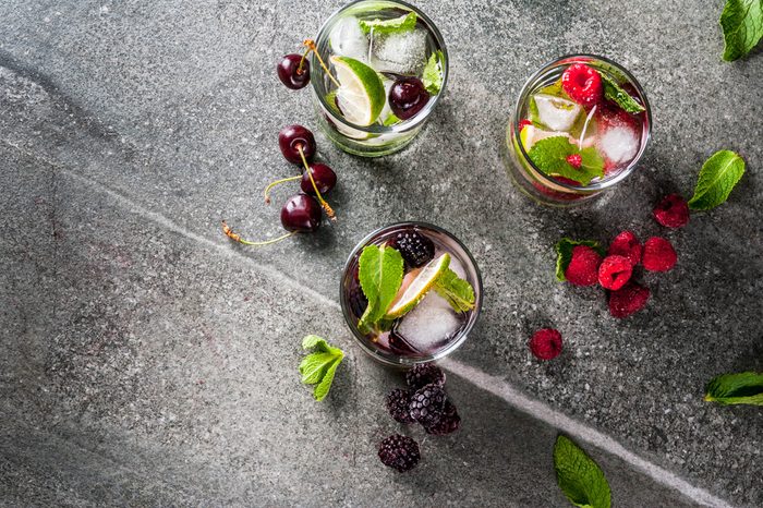 Set of traditional summer refreshing drinks berry mojito. With lime, mint leaves, blackberries, raspberries and cherries. With the ingredients on a dark stone table. Copy space top view