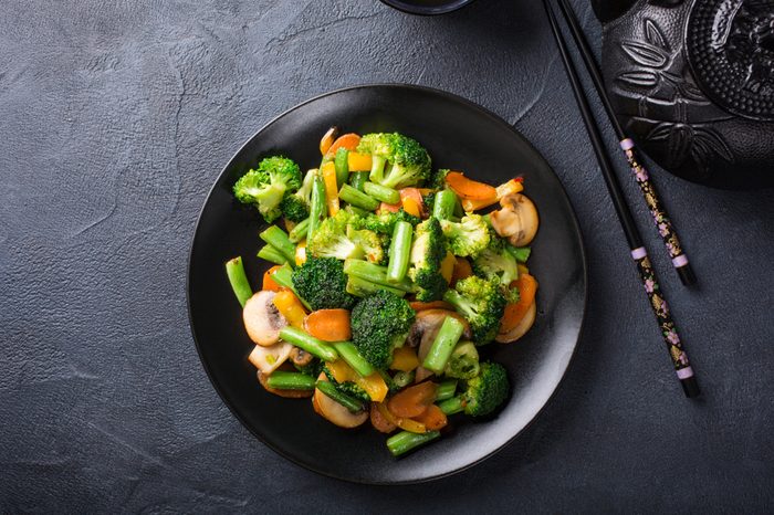 Hot stir fried vegetables on black plate. Healthy asian food concept with copy space.