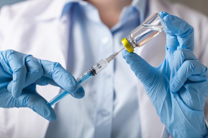 Hand holding syringe and vaccine.