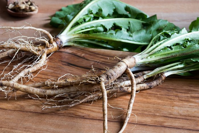 Dandelion roots with leaves on a wooden cutting board