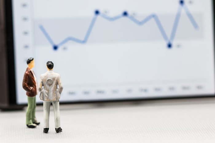 Miniature people : small figures businessmen stand with graph on the phone display with copy space and using as background finance business team competition concept, business plan concept.