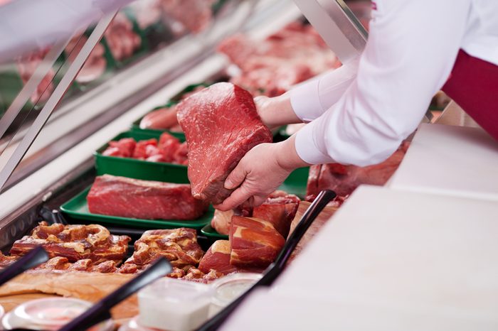 saleswoman offering fresh meat at display in supermarket
