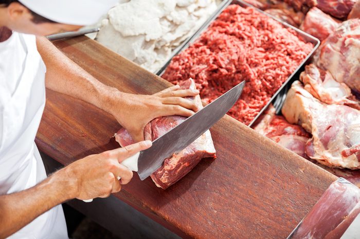 High angle portrait of smiling butcher cutting meat at counter in butchery
