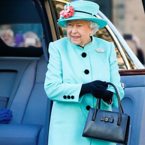 A woman in a turquoise outfit exits a car, holding a black handbag, outdoors in a formal setting.
