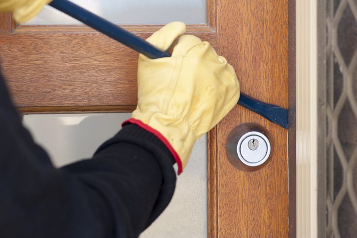 Burglar, thief with gloves, holding crowbar breaking into home, unlock door, copy space.
