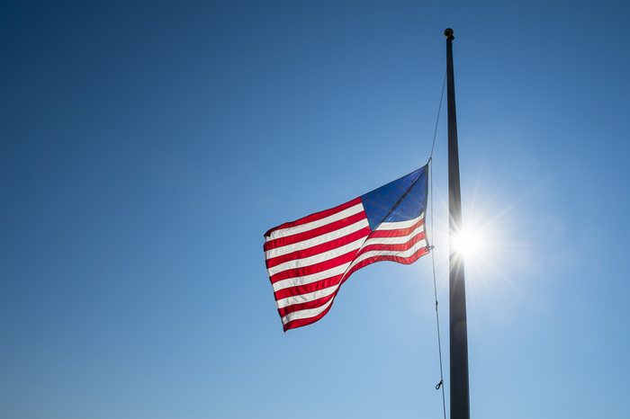 American flag lowered to half mast backlit by bright sun lens flare