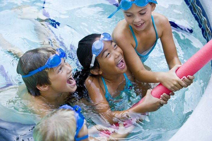 Four kids playing tug of war with pool toy, 7 to 9 years