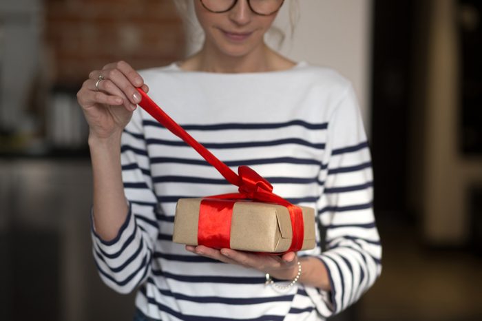 Female hands holding gift box with red ribbon. Woman opening her present. Casual style.
