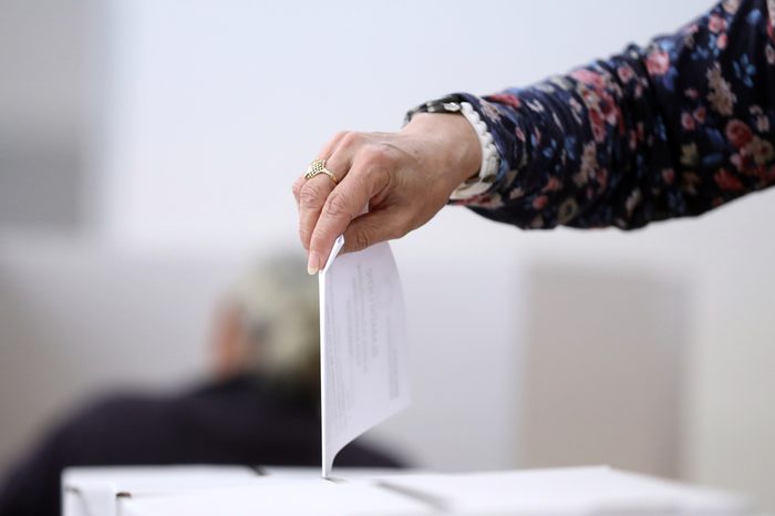 Woman hand casts a ballot as she votes for the local elections at a polling station. Focus on hand.