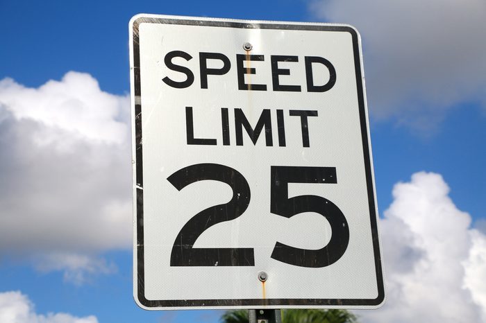Speed Limit 25 Mph Sign on a Bright Sunny Morning with Fluffy Clouds in the Background