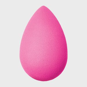 A pink, teardrop-shaped makeup sponge is standing upright against a plain white background.