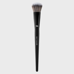 Makeup brush stands upright, displaying soft bristles and sleek black handle marked 