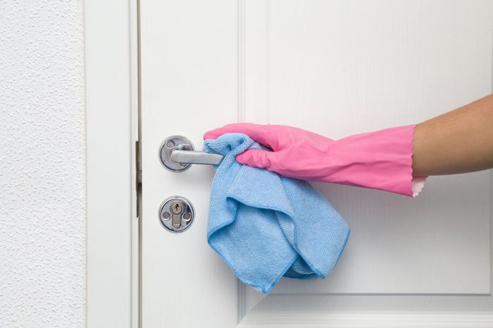 Employee's hand in rubber protective glove with rag wiping a door's handle. Maid or housewife cares about house. Spring general or regular clean up. Commercial cleaning company concept.