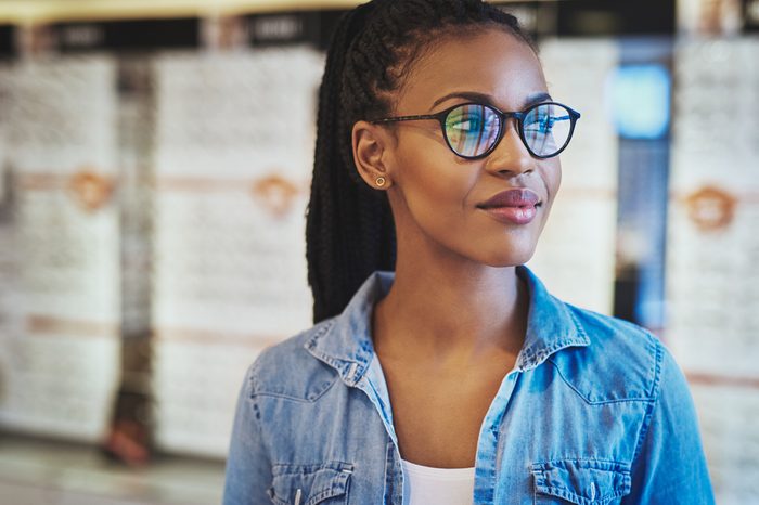 Single grinning young woman in casual shirt and eyeglasses looking over with copy space behind her
