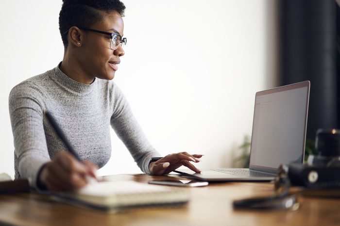 Young afro american female executive filling in application on official site of media marketing corporation ordering services and collaboration via laptop computer and wireless internet indoor