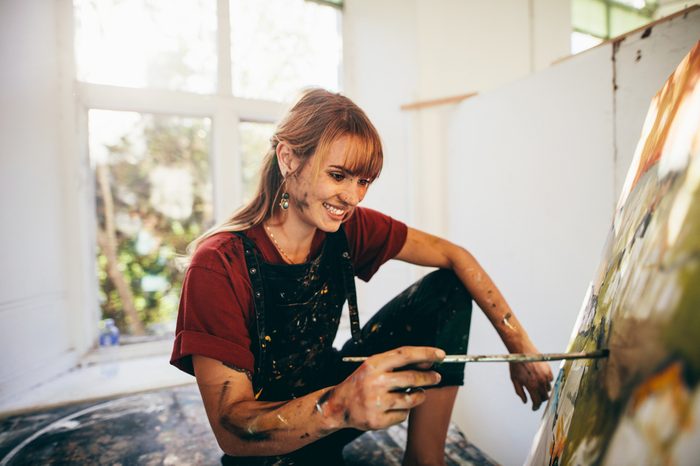 Indoor shot of professional female artist painting on canvas in studio. Woman painter painting in her workshop.