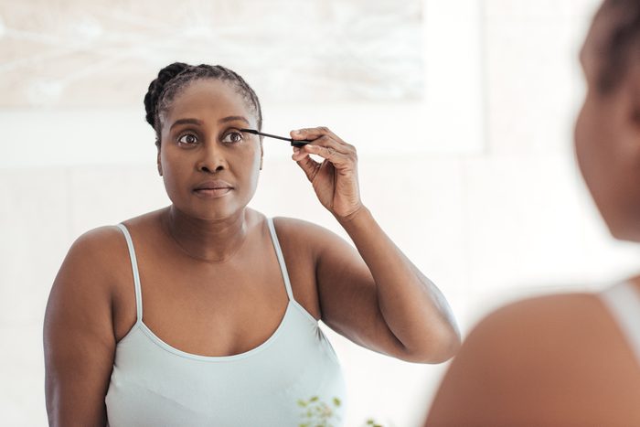 Young African woman standing in her bathroom in the morning applying mascara to her eyelashes in a mirror