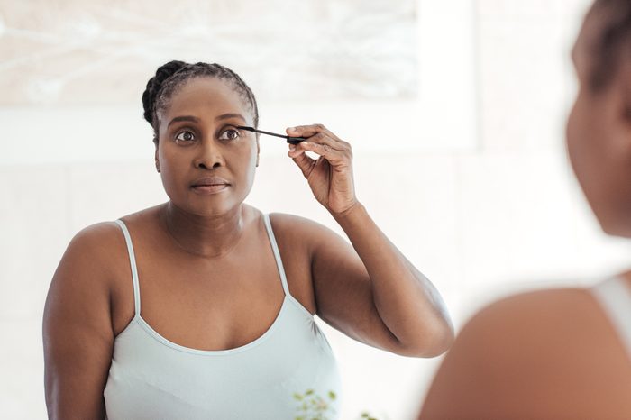 Young African woman standing in her bathroom in the morning applying mascara to her eyelashes in a mirror